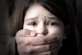 Scared young girl with an adult man's hand covering her mouth.